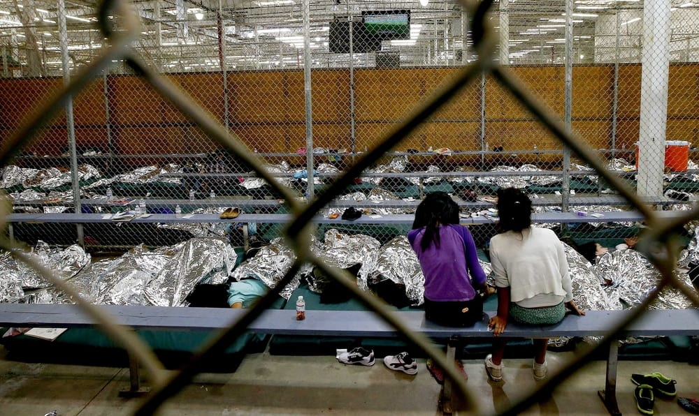 Two young girls watch a World Cup soccer match on a television from their holding area where hundreds of mostly Central American immigrant children are being processed and held at the U.S. Customs and Border Protection Nogales Placement Center on June 18, 2014, in Nogales, Arizona. (Photo by Ross D. Franklin-Pool/Getty Images)
