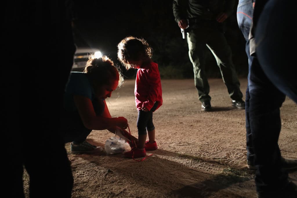 A Honduran mother removes her two-year-old daughter's shoe laces, as required by U.S. Border Patrol agents, after being detained near the U.S.-Mexico border on June 12, 2018 in McAllen, Texas. (Getty Images)