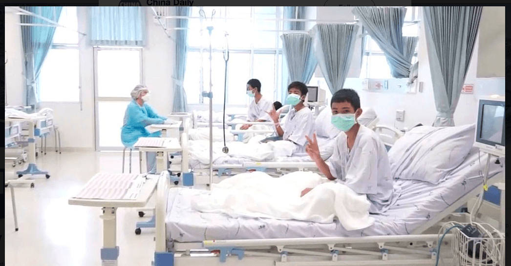 The rescued boys waving at the camera from their hospital beds in a first appearance after being rescued. (Twitter)