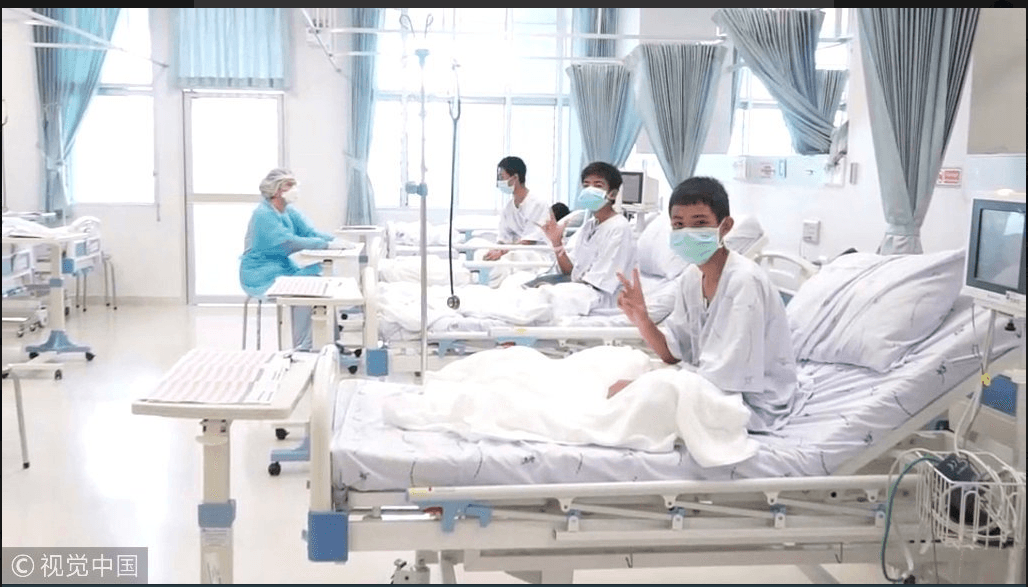 The boys smiling and waving at the camera from their hospital beds after being rescued. (Twitter)