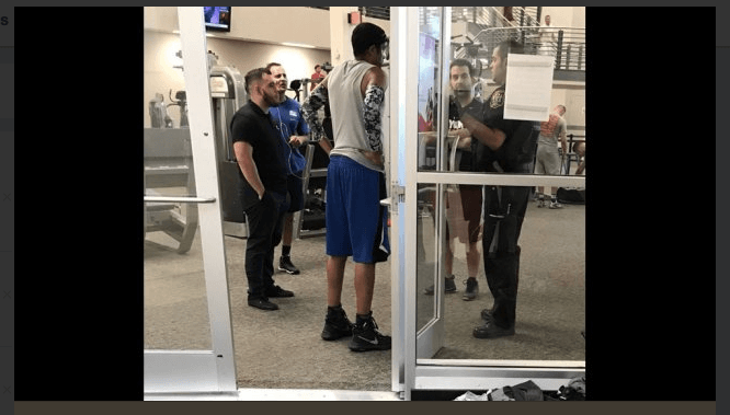 The black man standing (C) while the white man (R) and the cop (extreme right) can be seen on the other side of the door. (Twitter)